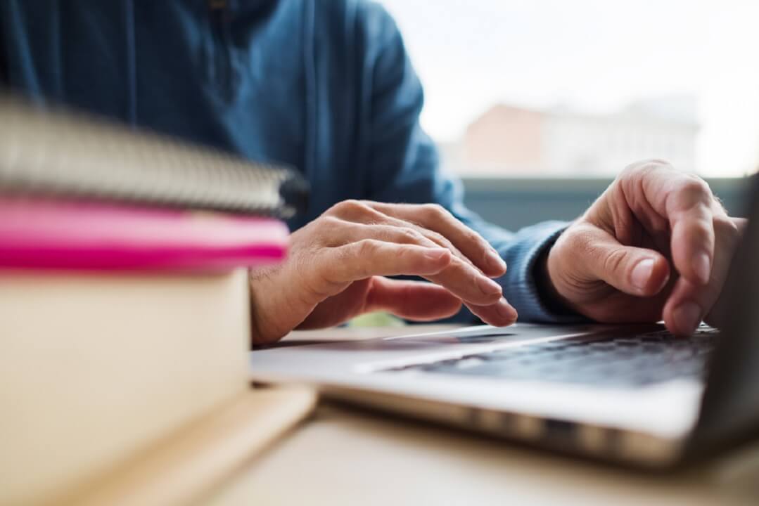 man typing on a laptop studying on table with books