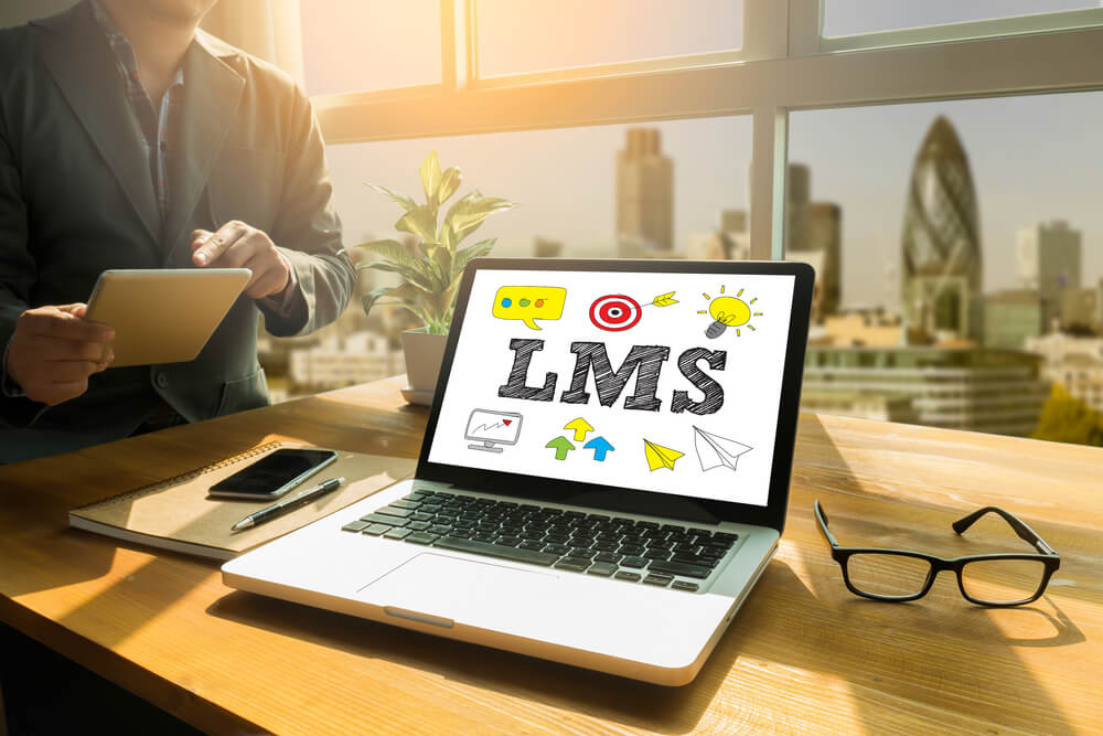 laptop showing LMS with man holding tablet in background