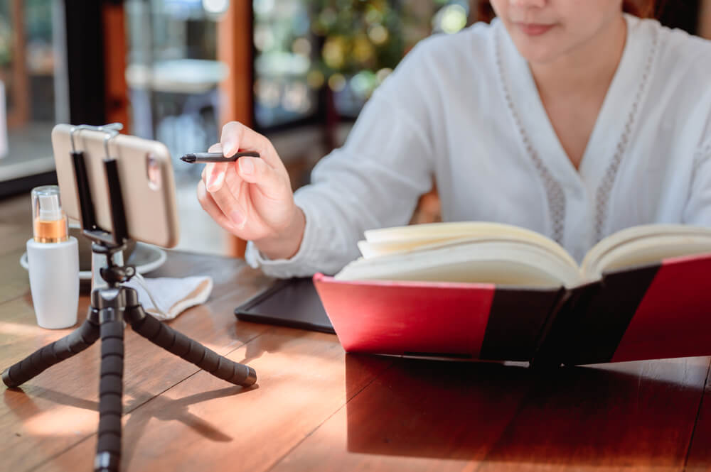A woman reading a book while using a cellphone to get access to online learning resources