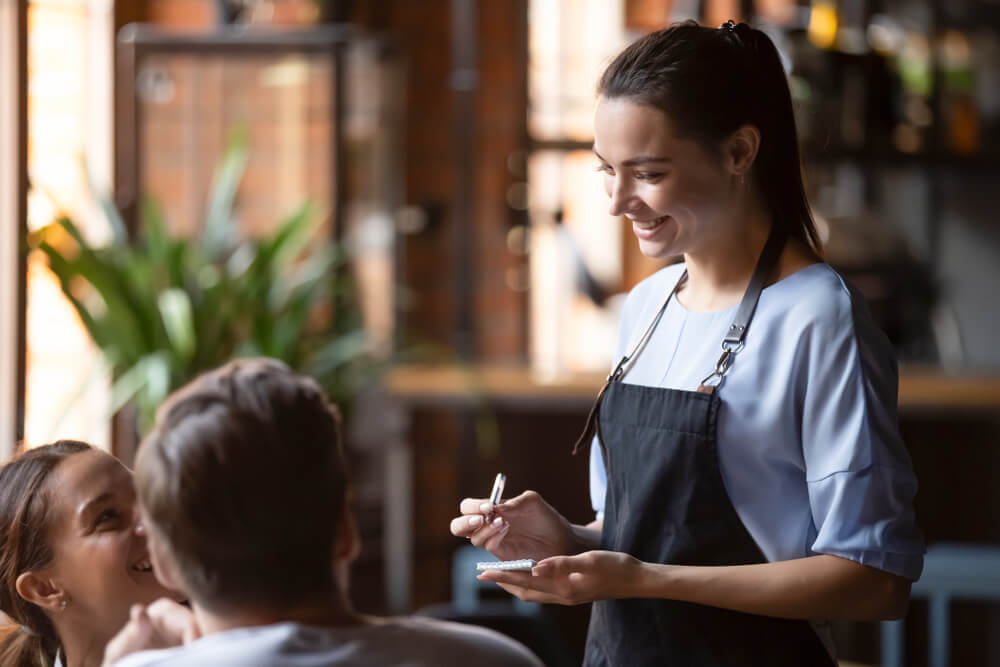 female waitress smiling at guests and jotting down orders