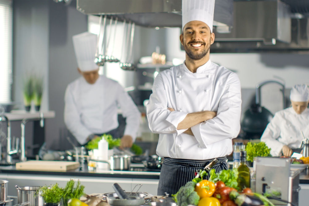 young male chef with crossed arms smiling in commercial kitchen