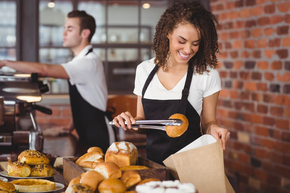 smiling waitress putting bread roll in paper bag