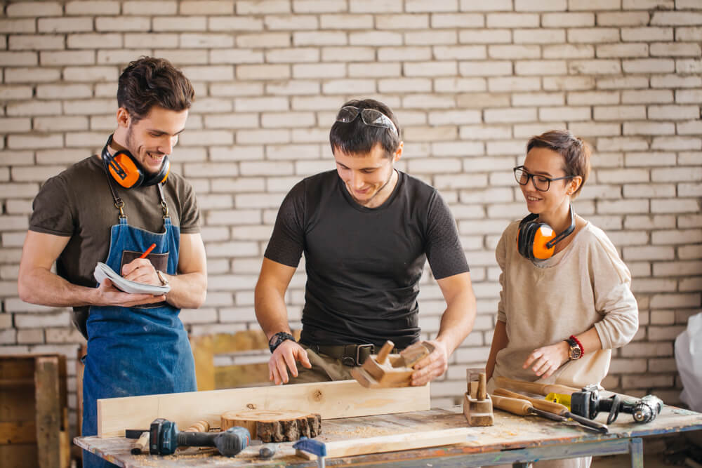 young male carpenter teaching students in woodworking workshop
