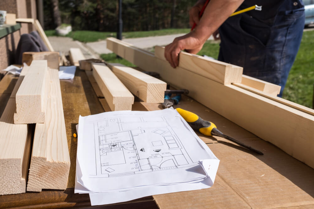 closeup of carpenter measuring wood, following technical blueprint