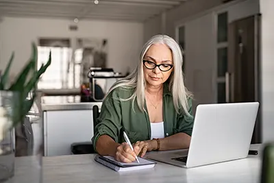 Senior woman taking notes while using the laptop for an online learning program